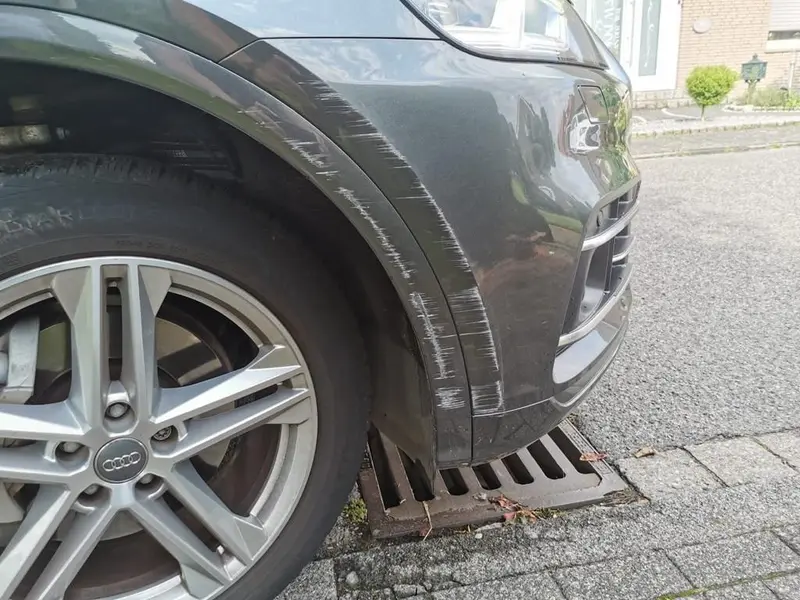 Vorher: tiefe Kratzer an Stoßfänger und Radlauf eines grauen SUV